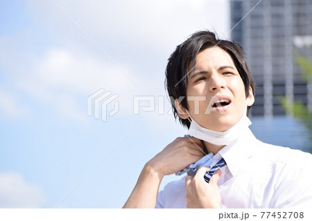 暑くてマスクを外してハンカチで汗を拭いている若い男性 暑くてマスクを外してハンカチで汗を拭いている若い男性 77452708