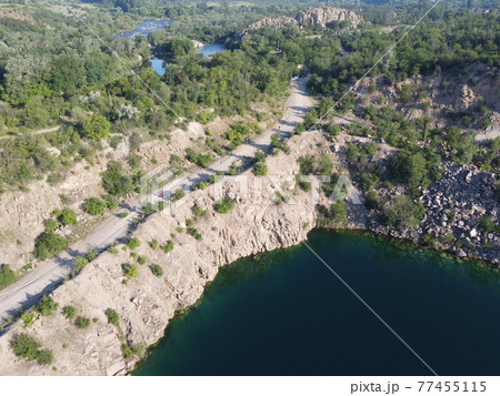 Rocky shore of the Radon Lake on a sunny summer morning. Aerial view of an old flooded granite quarry. A picturesque pond. 77455115
