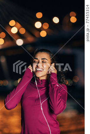 Female runner listening to music on earphones at night 77455314