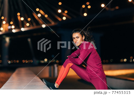 Woman stretching before an evening run. Young female jogger warming up legs at night. Woman stretching before an evening run. Young female jogger warming up legs at night. 77455315