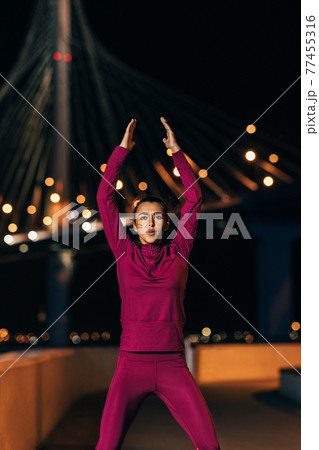 Female athlete in front of bridge at night. Woman wearing sportswear warming up body in the city in the evening. Female athlete in front of bridge at night. Woman wearing sportswear warming up body in the city in the evening. 77455316