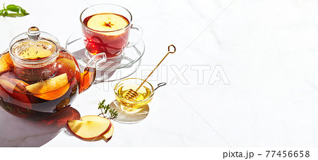Fruit tea with apples and thyme and honey in glass teapot and cup on white background with hard shadows 77456658