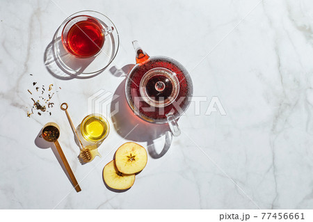 Fruit tea with apples and thyme and honey in glass teapot and cup on white background with hard shadows Fruit tea with apples and thyme and honey in glass teapot and cup on white background with hard shadows 77456661