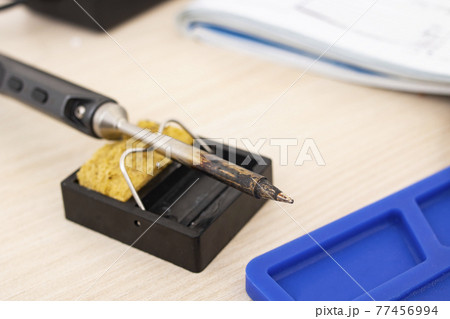 Soldering iron on a stand on the desktop 77456994