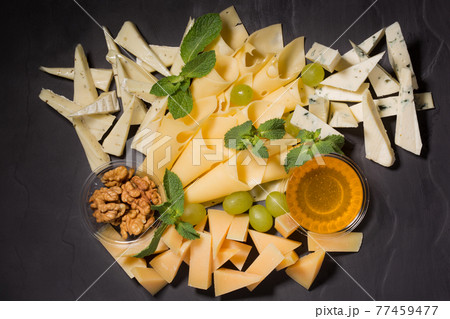 assorted cheese on black slate, nuts and honey, decorated with grapes and mint leaves assorted cheese on black slate, nuts and honey, decorated with grapes and mint leaves 77459477