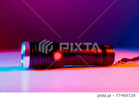 A small black flashlight in colored lighting. A small black flashlight in colored lighting. 77460726