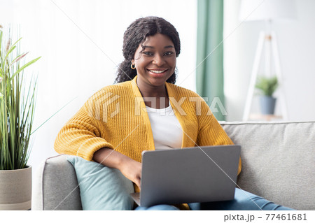 Cheerful young black woman freelancer working from home, using laptop 77461681