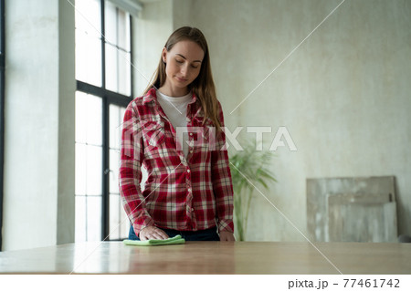 Young woman wipes a table with a rag at home. Concept of homework and household management 77461742