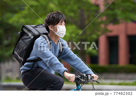 自転車で走行するマスク姿の配達員 自転車で走行するマスク姿の配達員 77462302