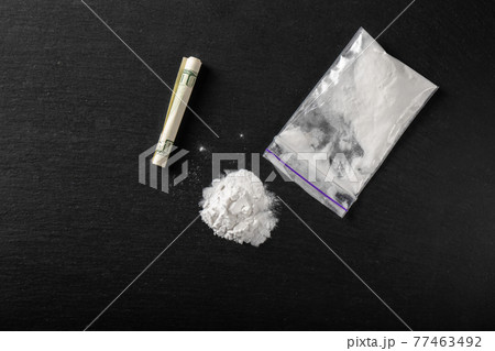Cocaine in a plastic package on a black background, close-up. A rolled up dollar bill for drug use. 77463492