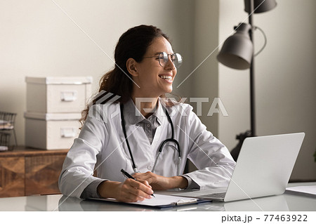 Smiling millennial latin woman doctor distracted from paperwork thinking dreaming 77463922