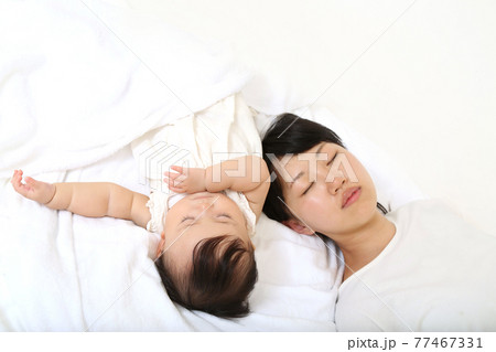 白いシーツの背景で赤ちゃんと一緒に昼寝をするお母さん 77467331