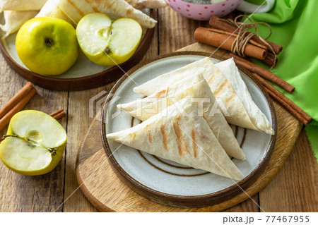 Apple pastries for breakfast. Grilled lavash triangle with apples and cinnamon on a wooden wooden table. 77467955