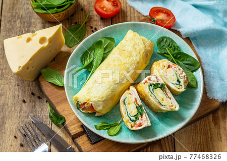 Japanese cuisine. National Japanese dish Omelet tamago yaki for breakfast. Rolled egg with spinach, tomato and cheese on a wooden table. 77468326