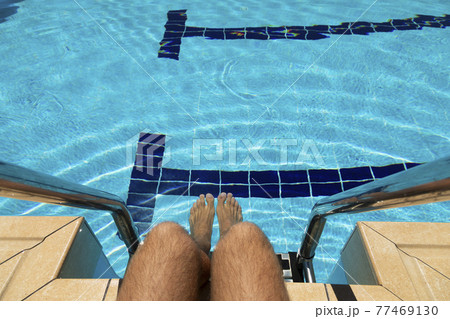 The feet of a young man in a swimming pool in summer, Spain. 77469130