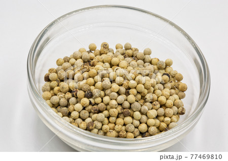 white pepper seeds in a glass bowl closeup against white 77469810