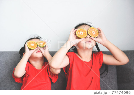 Little girl playing with fresh mandarin orange fruits child is having fun with fruit food for kids funny time at home, happy cute girl kids food eating concept 77474096