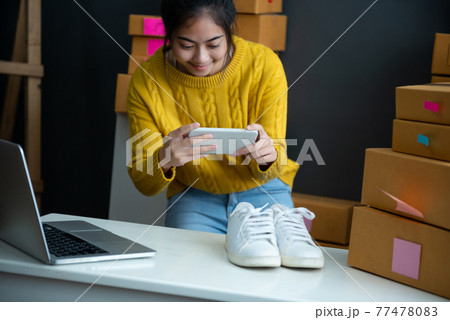 asian smiling girl using smartphone to shoot white sneaker posted for sale on the internet 77478083