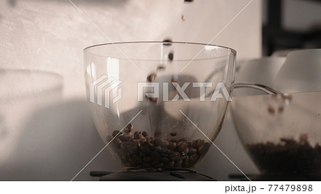 fresh coffee beans falling into coffee grinder hopper 77479898
