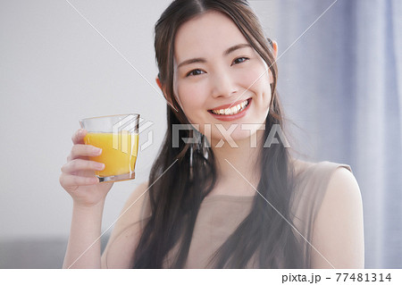 リビングでオレンジジースを飲む若い女性 リビングでオレンジジースを飲む若い女性 77481314