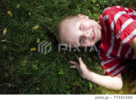 A happy boy lies in the grass, stroking her and looking at the sky. Sometimes something says or points a finger to the top. The concept of a family holiday in the park and happy childhood. 77482886