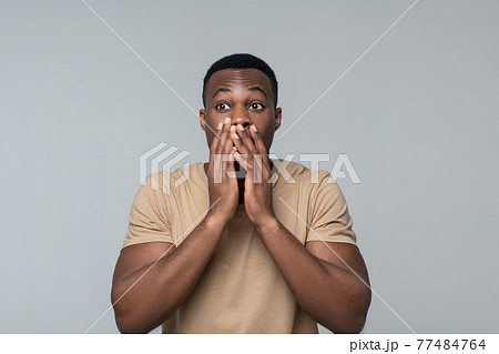 Amazed dark skinned man touching mouth with hands 77484764