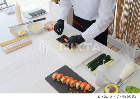 Male chef in uniform peeling avocado for sushi Male chef in uniform peeling avocado for sushi 77486085