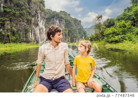 Dad and son tourists in boat on the lake Tam Coc, Ninh Binh, Viet nam. It's is UNESCO World Heritage Site, renowned for its boat cave tours. It's Halong Bay on land of Vietnam. Vietnam reopens borders 77487346