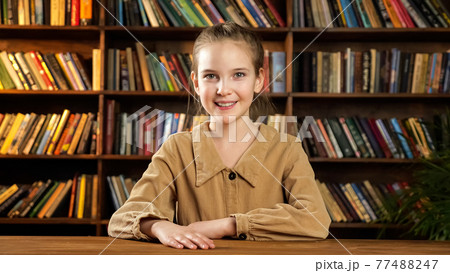 Schoolgirl model poses sitting at new brown wooden desk Schoolgirl model poses sitting at new brown wooden desk 77488247
