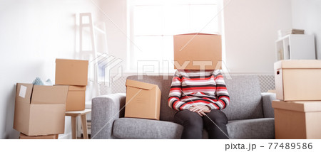 Tired womanwith cardboard box on her head sitting on the sofa in her new house. Tired womanwith cardboard box on her head sitting on the sofa in her new house. 77489586