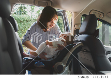 Asian young mother putting her baby son into car seat Asian young mother putting her baby son into car seat 77491031