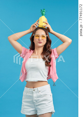 excited Asian girl holding pineapple over her head and smiling at camera isolated on blue background excited Asian girl holding pineapple over her head and smiling at camera isolated on blue background 77491172