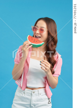 Attractive Asian young woman wearing summer vest and holding the Piece slide of watermelon on isolated blue color background, 77491201
