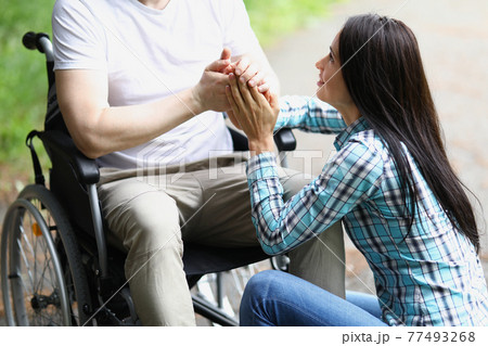 Disabled man in wheelchair holding woman hands in park closeup Disabled man in wheelchair holding woman hands in park closeup 77493268