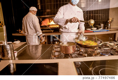 Chef adding sauce to vegetables in cooking pan 77497486