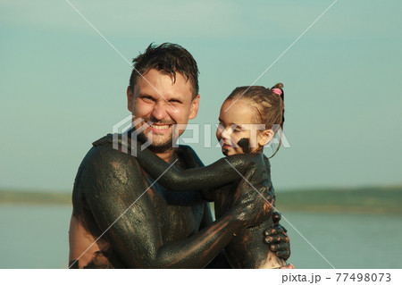 therapeutic mud for the body. mud baths on the lake. a man and a child are smeared with clay. family at the resort therapeutic mud for the body. mud baths on the lake. a man and a child are smeared with clay. family at the resort 77498073