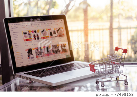 Online shopping concept - shopping cart or trolley and laptop on table Online shopping concept - shopping cart or trolley and laptop on table 77498158