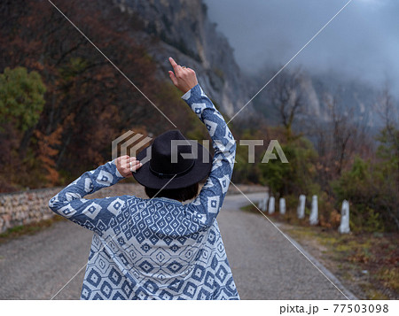 Stylish hipster woman in a hat walking down a mountain road Stylish hipster woman in a hat walking down a mountain road 77503098