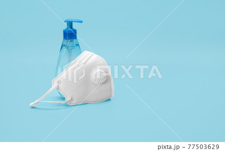 Protective medical mask and sanitizer on a blue background. A set for prevention against coronavirus infection. Personal hygiene. 77503629
