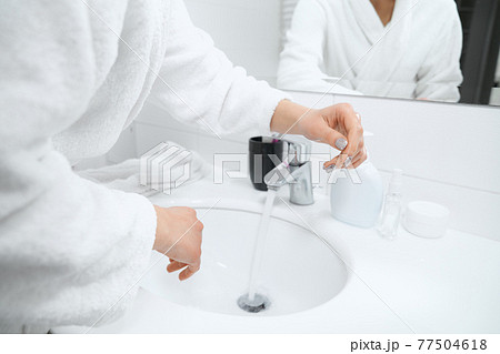 Woman in white robe standing near sink and washing hands. Woman in white robe standing near sink and washing hands. 77504618