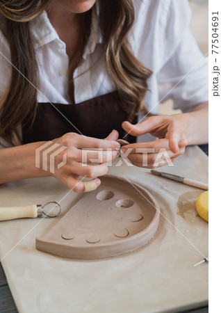 Artisan female potter prepares material for her pottery. Woman hands attach clay part to future ceramic product. Work close-up. Artisan female potter prepares material for her pottery. Woman hands attach clay part to future ceramic product. Work close-up. 77504691