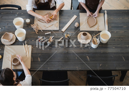 Young women learning to sculpt with a clay during a lesson at workshop in art studio. 77504710