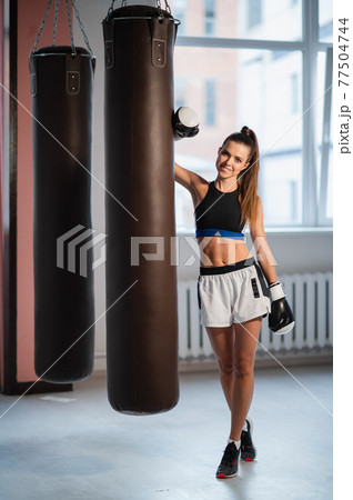 Female athlete boxing the punching bag in urban industrial gym 77504744