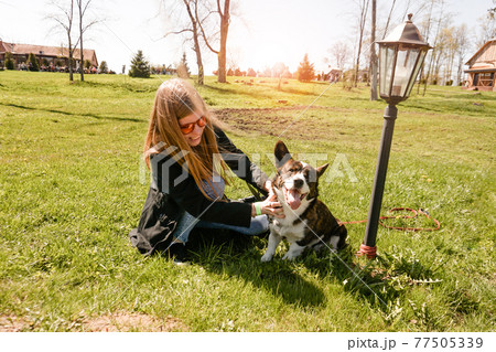 Young woman in red sunglasses plays with her corgi on a summer green lawn Young woman in red sunglasses plays with her corgi on a summer green lawn 77505339
