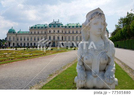 VIENNA, AUSTRIA - APR 30th, 2017: Upper Belvedere Palace with a close-up of a statue of a horse at the entrance on a sunny day with blue sky and clouds in summer and tourists walking 77505880
