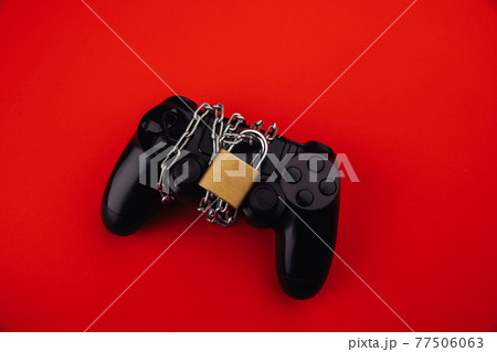 Gamepad with chain and padlock on red background, game addiction concept. 77506063