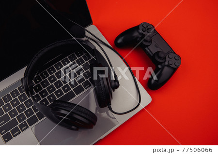 Gaming and cybersport concept. Laptop with headphones and black gamepad on red background 77506066
