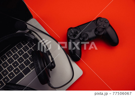Laptop with headphones, black gamepad on red background. Gaming and cybersport concept 77506067