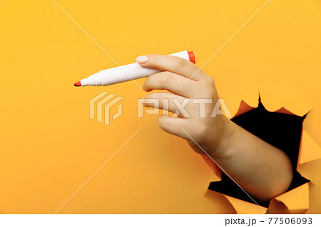 A female hand with marker though a broken yellow paper wall 77506093