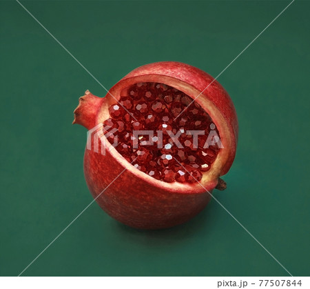 Beautiful red sliced pomegranate on a green background. Pomegranate fruit with red shiny beads, garnet crystals instead of seeds and grains. Macro, close up, abstraction. Jewelry unusual fruit. 77507844